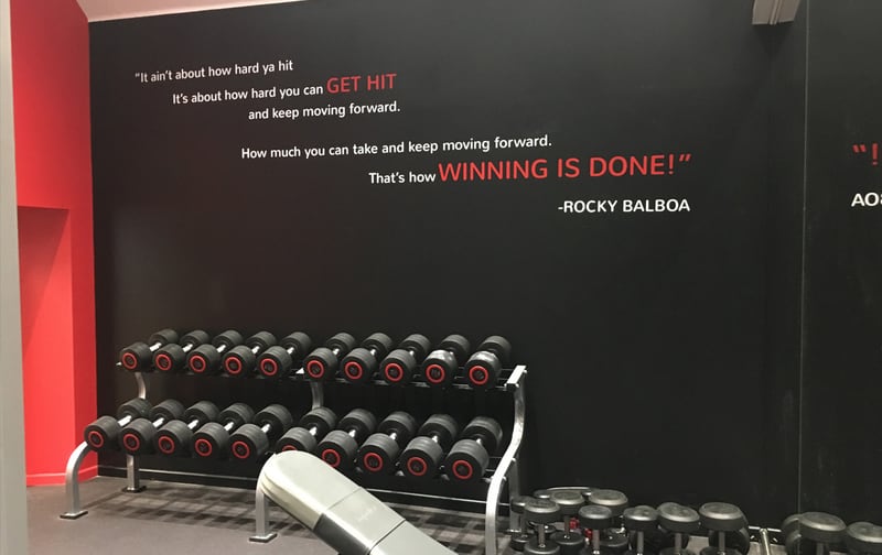 Dumbbell rack under a Rocky Balboa quote on the wall